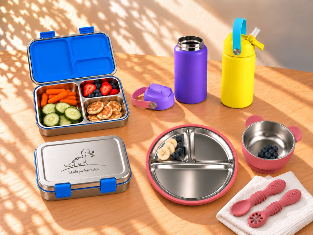 Open gevulde en dichte RVS bento met dino, drinkflessen, kinderbord, beer-kommetje en oefenlepeltjes op een houten tafel
